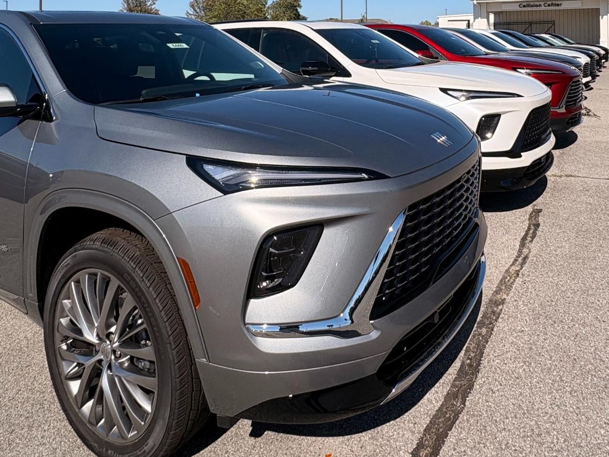 A lineup of new Buick SUVs parked outside a dealership, including silver, white, and red models shown in a front-angle view.