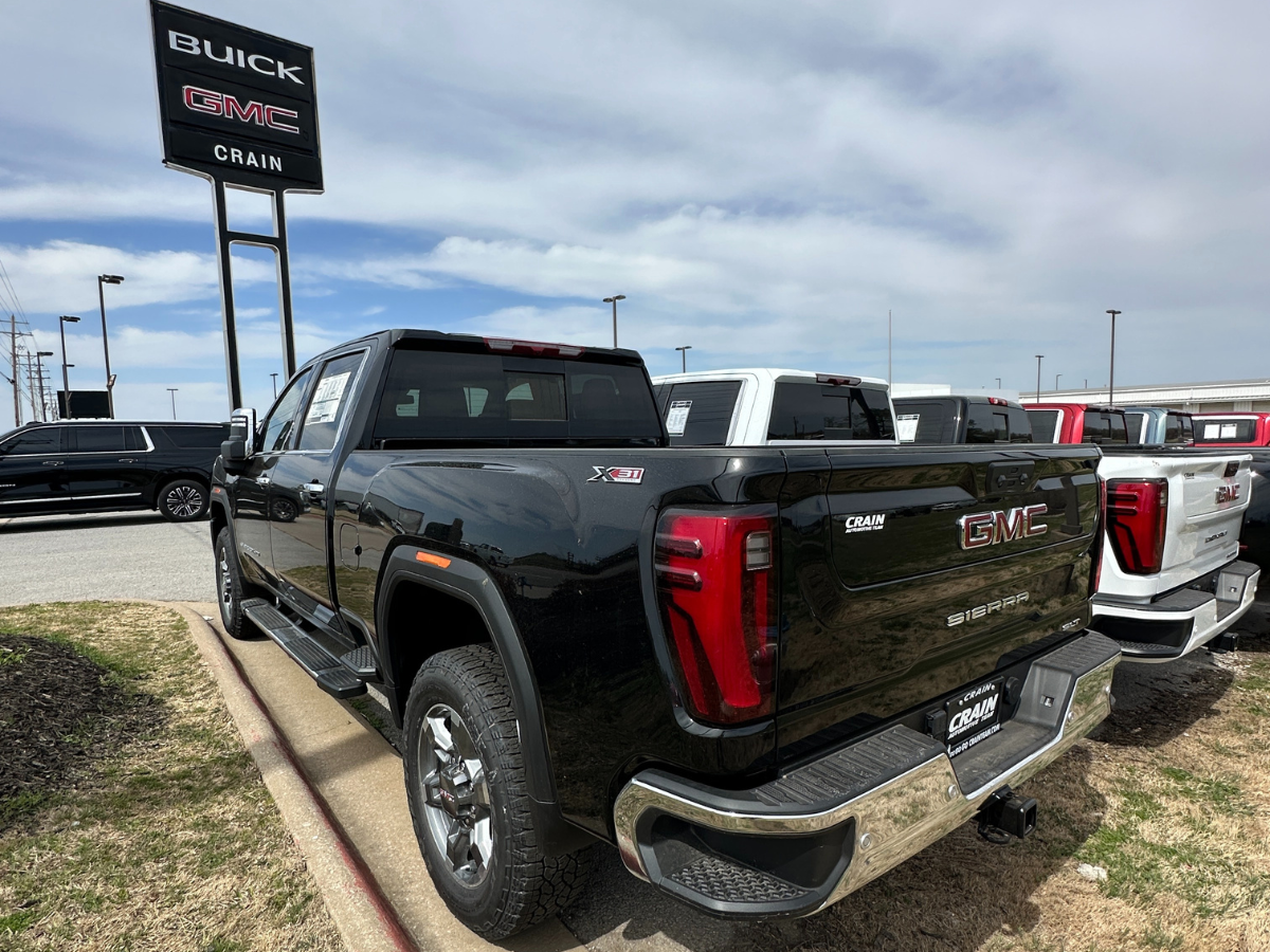 Rear and side view of a black 2024 GMC Sierra X31 parked at Crain Buick GMC in Springdale, Arkansas, with other new trucks in view