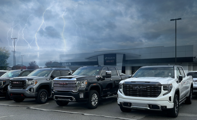 Row of GMC trucks parked at Crain Buick GMC in Springdale with storm clouds and lightning in the background
