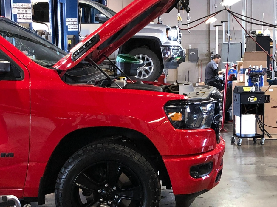 Technician working in service bay with red truck and silver GMC in background at Crain Buick GMC in Springdale, Arkansas