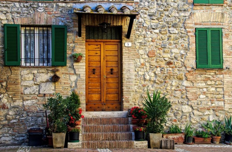 Stone cottage with green shutters and potted plants in front of a wooden door