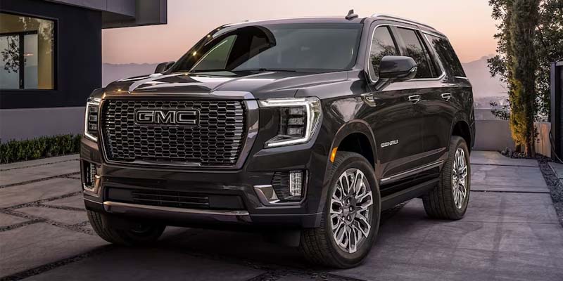 Front view of a black 2023 GMC Yukon XL parked in a modern driveway at sunset