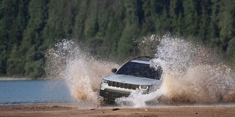 2026 Jeep Cherokee splashing through water on an off-road trail, demonstrating its off-road capabilities and rugged performance.