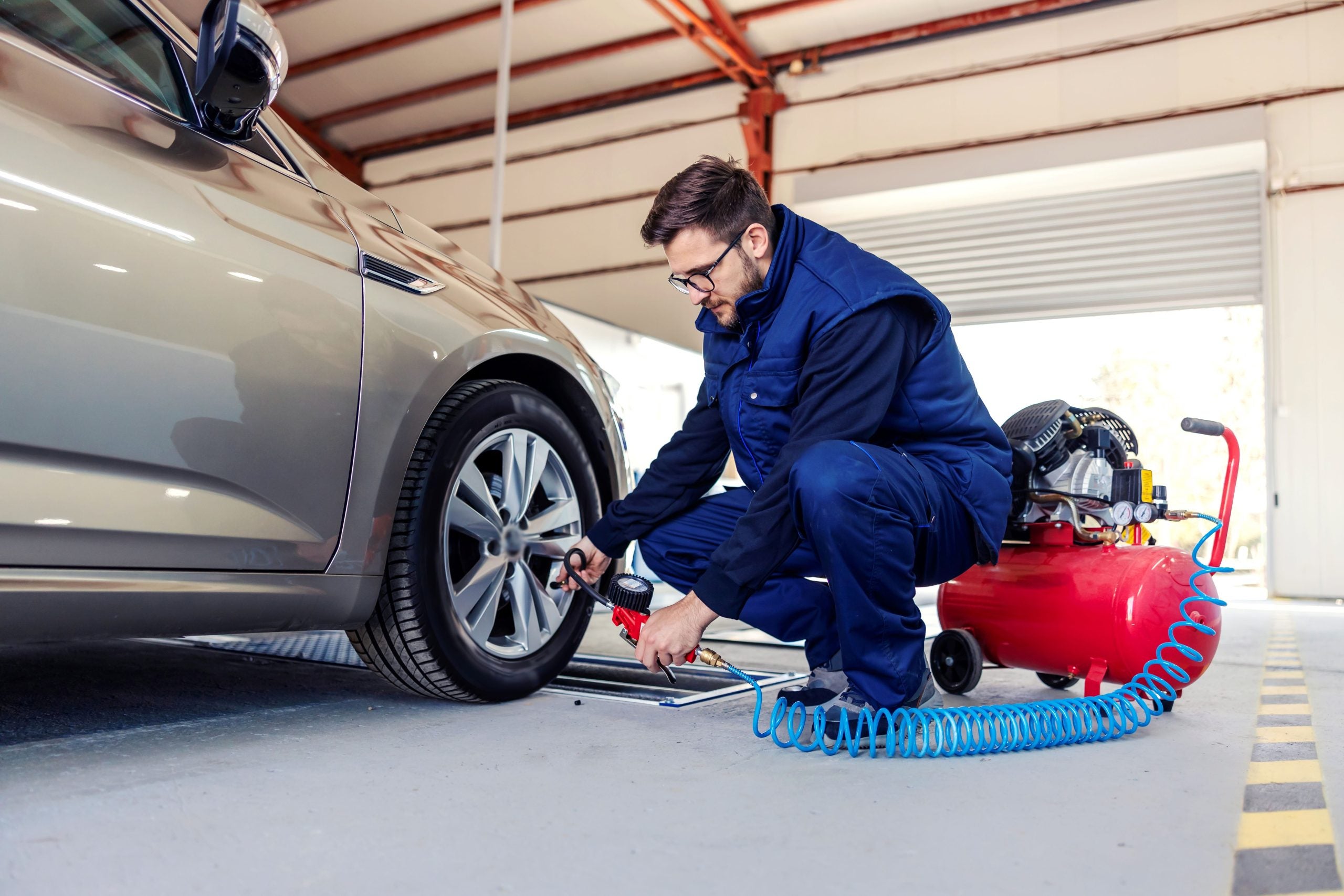 A technician inflating a car tire using an air compressor in a service garage.