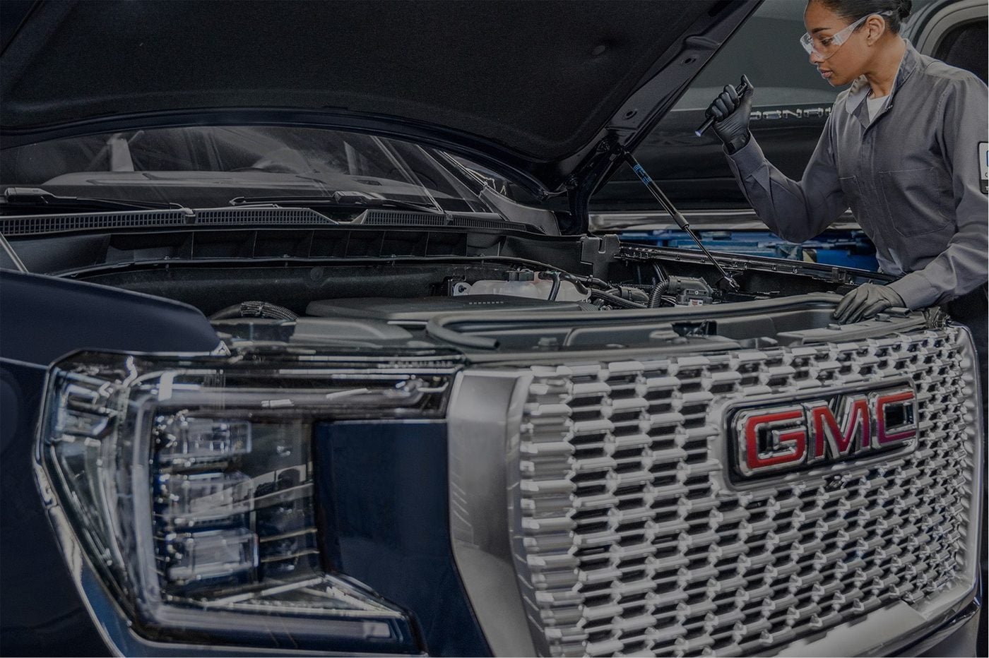 Technician working under the open hood of a GMC Denali in the Holiday GMC service bay in Graham, TX