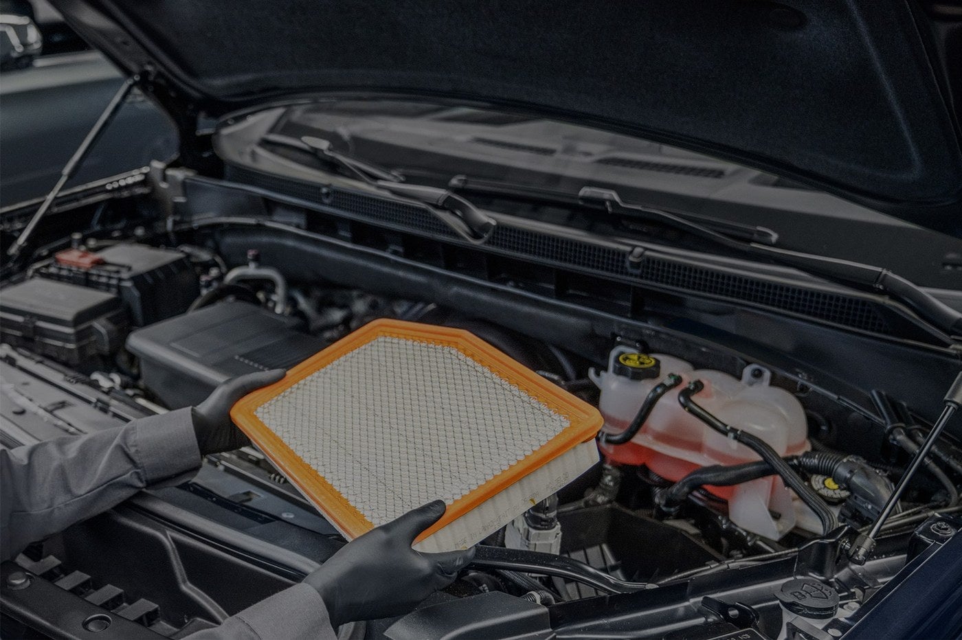 Technician holding a new engine air filter over a GMC engine bay during service in Graham, TX