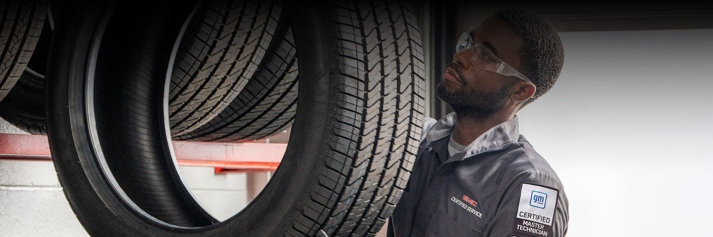 GM certified technician holding a tire next to tire storage racks at a GMC dealership in Graham, TX