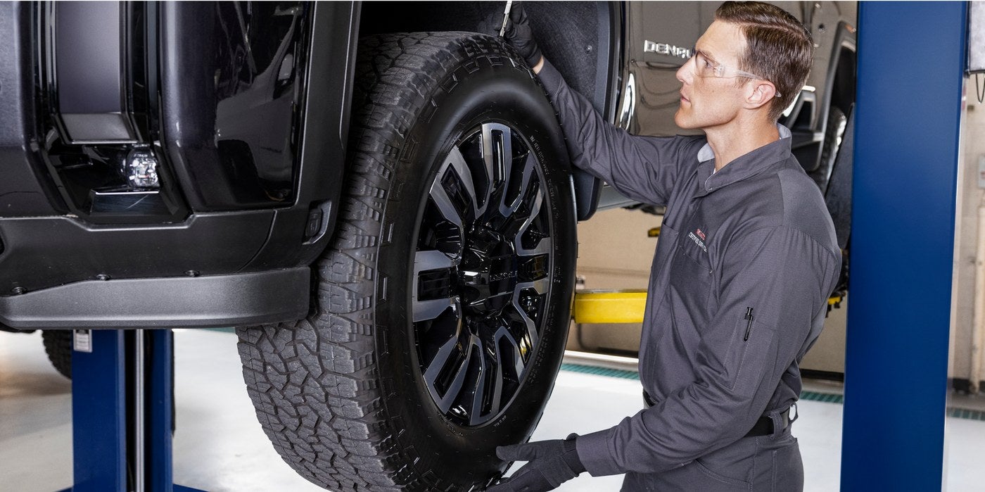Technician working on a GMC truck tire while the vehicle is raised on a lift