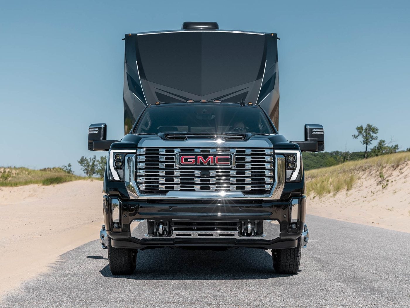 Front view of a GMC Sierra HD hauling a large RV trailer down a sandy road
