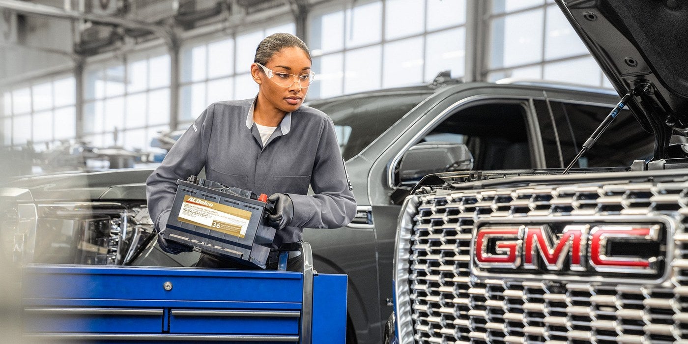 GMC technician with a diagnostic tablet next to a Denali grille in the Holiday GMC service department