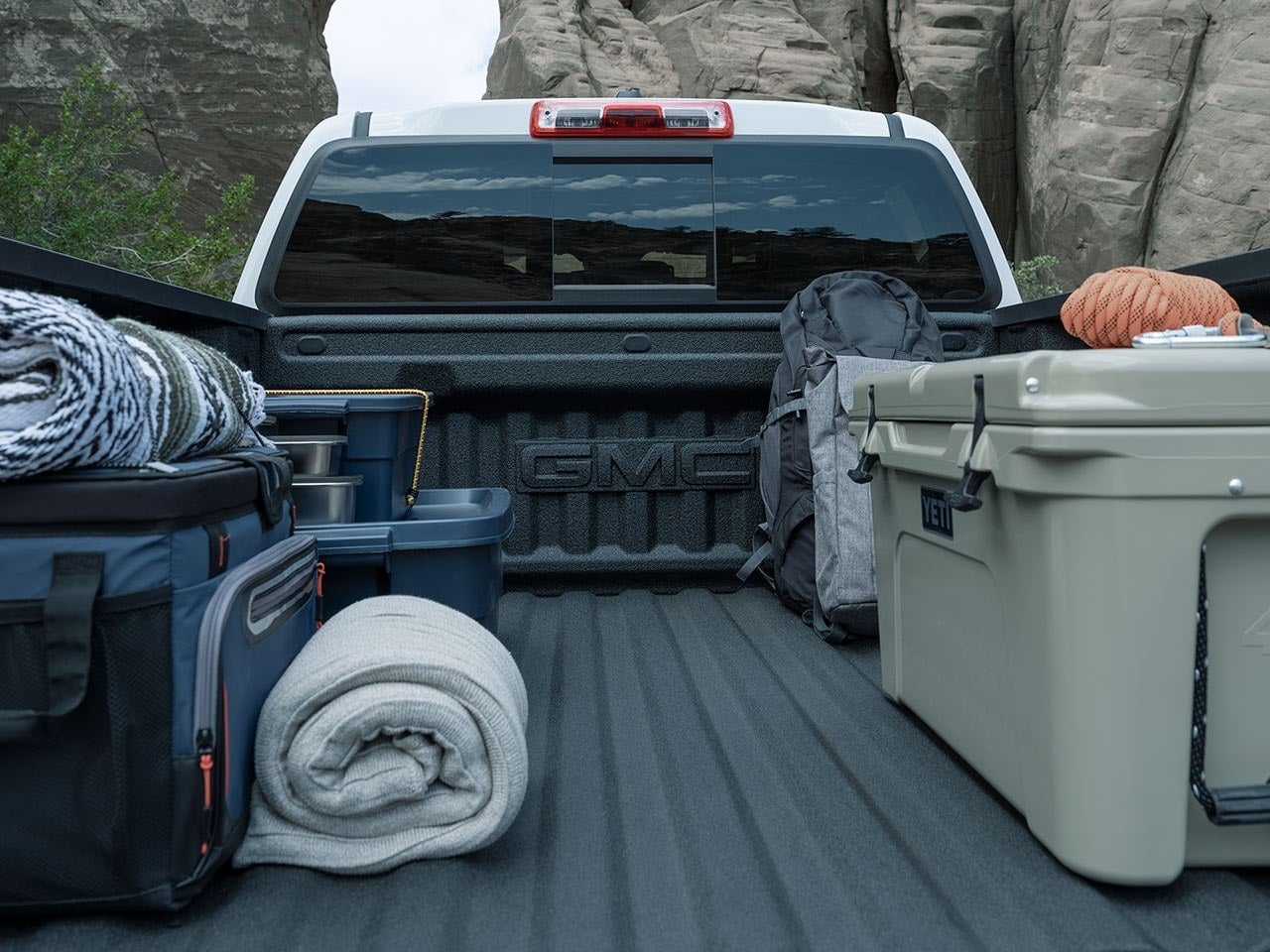 Bed of a GMC Canyon loaded with a cooler, bedroll and camping gear