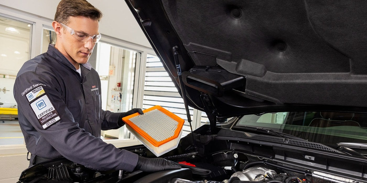 Technician holding an engine air filter over a GMC engine in the service department