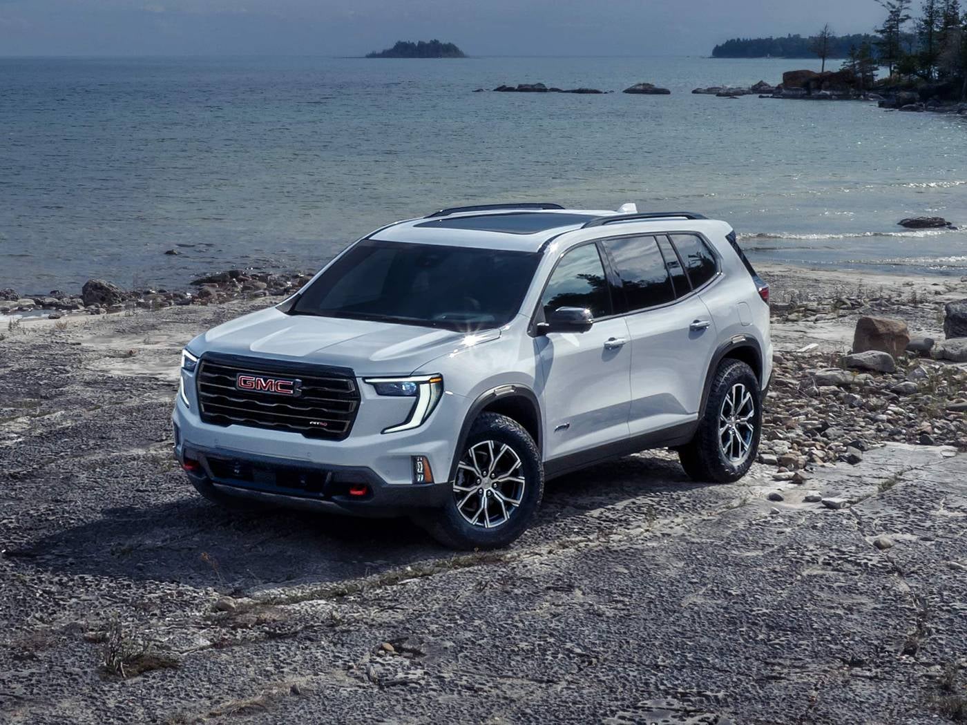 White GMC Acadia SUV parked on a rocky shore beside the water