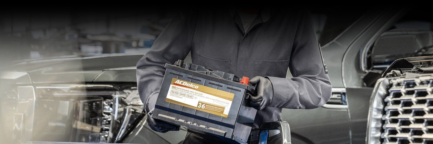 Technician holding an ACDelco battery in front of a GMC truck during a battery replacement