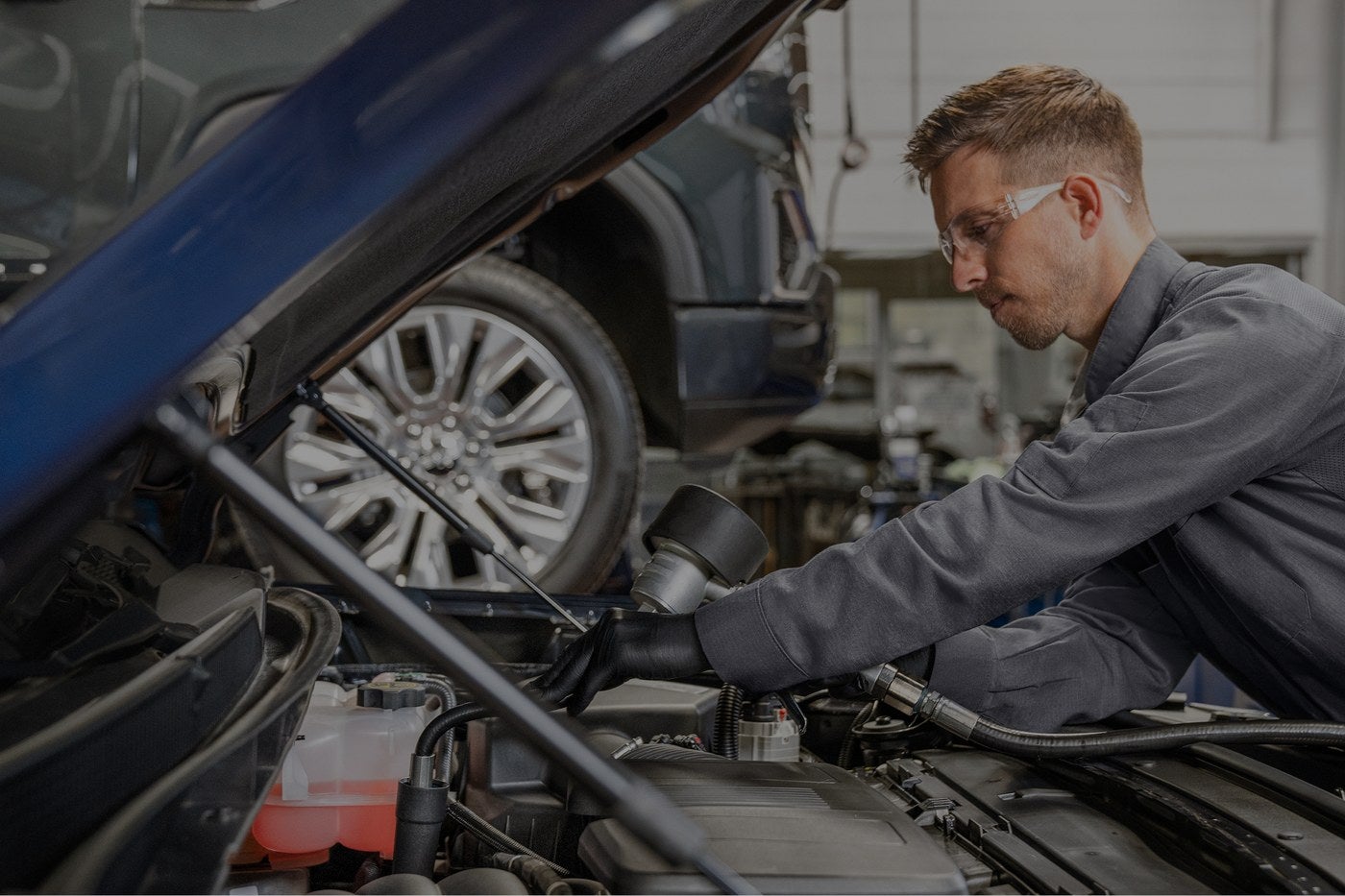 Technician working under the open hood of a GMC truck in the service bay