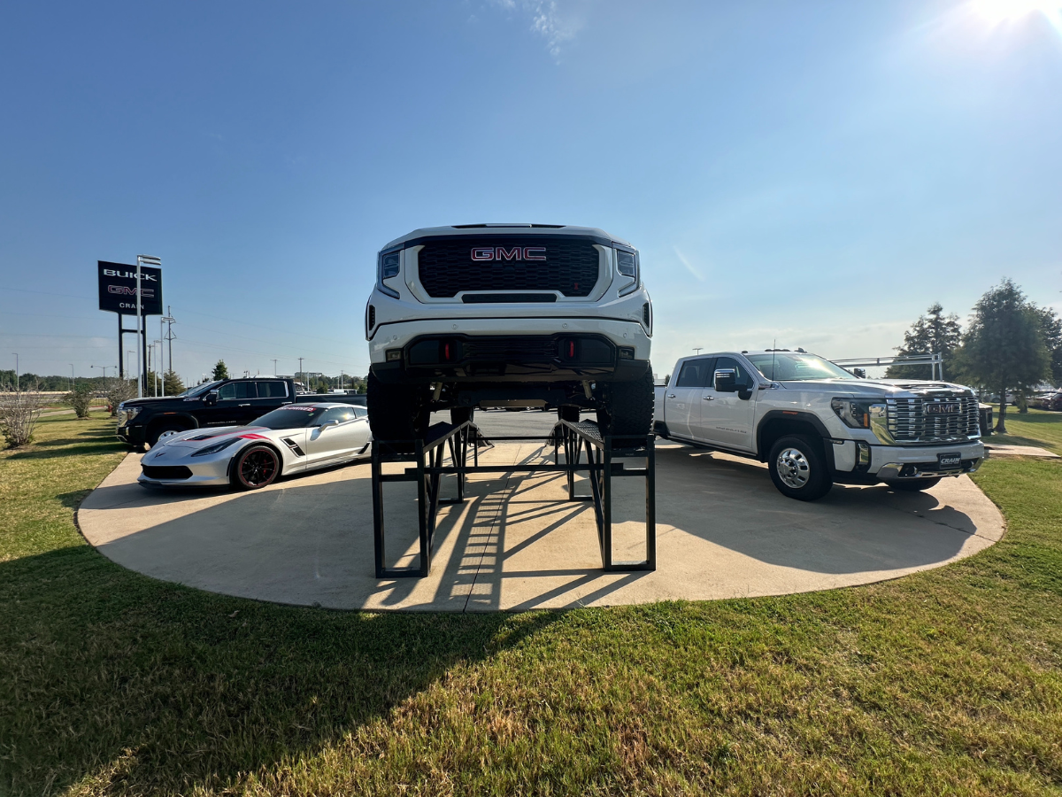 Display of used and lifted GMC trucks and sports cars at Crain Buick GMC in Conway, Arkansas under a sunny sky