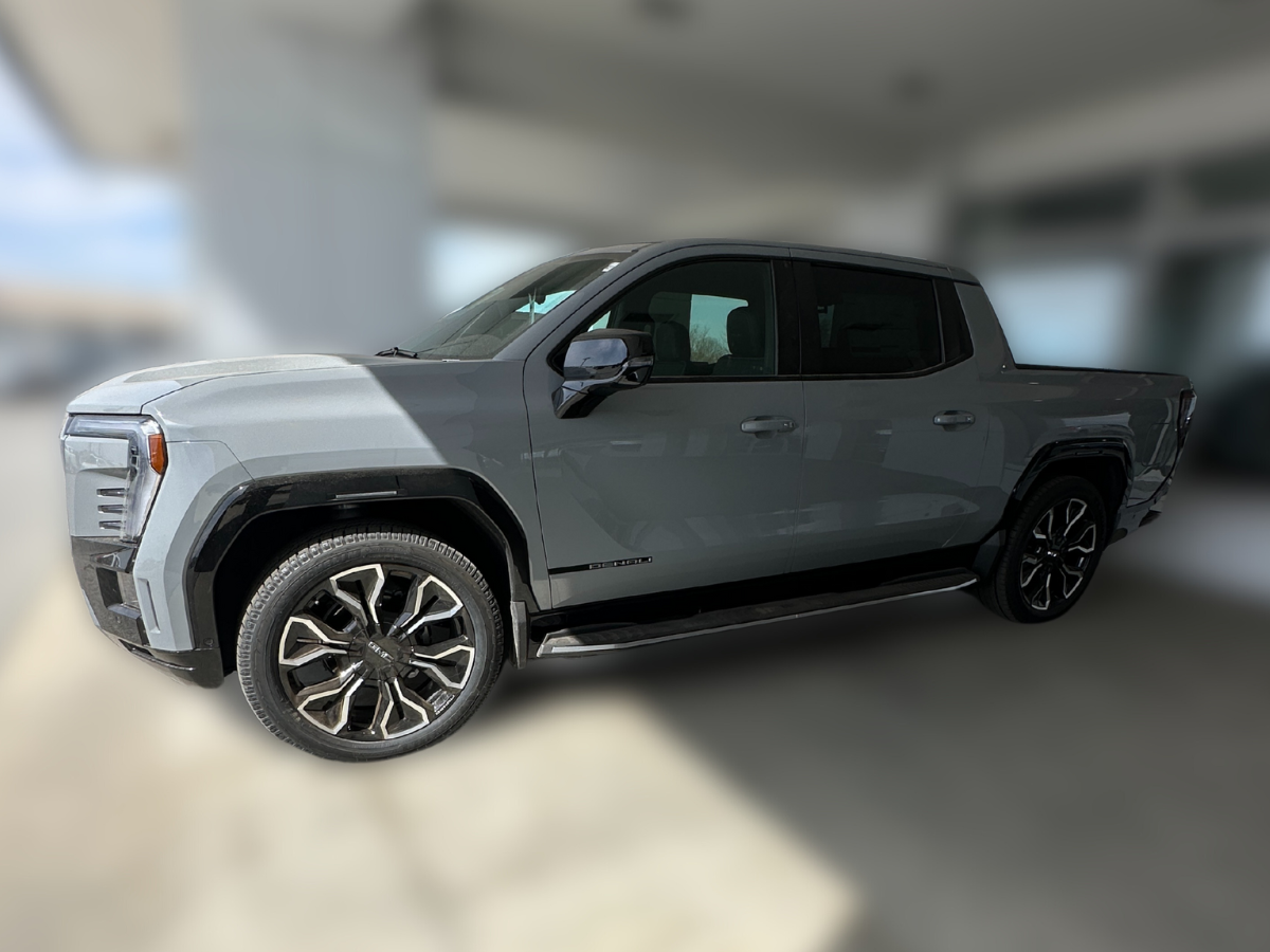 Side profile of the all-new 2026 GMC Sierra EV pickup truck in gray, parked in a dealership delivery area
