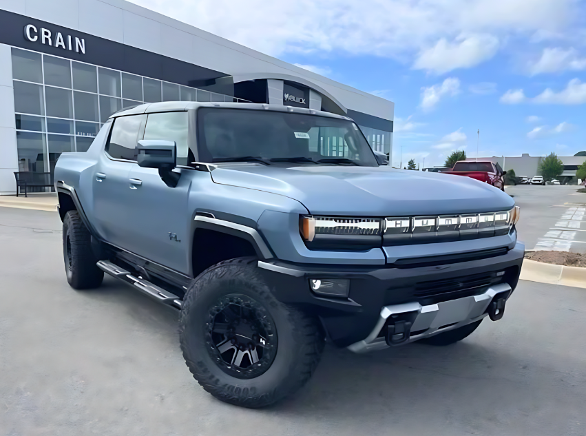 Front and side view of a matte blue GMC Hummer EV pickup parked in front of Crain Buick GMC in Conway, Arkansas