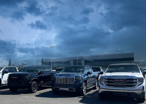 Lineup of GMC trucks under a stormy sky with lightning, parked at Crain Buick GMC in Conway, Arkansas