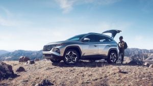 A woman standing behind a parked, silver 2022 Hyundai Tucson. | Hyundai dealer in North Little Rock, AR.