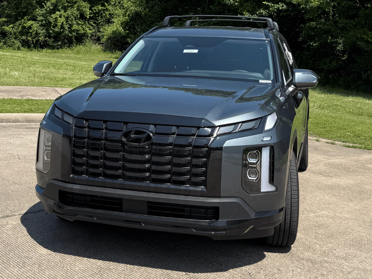2025 Hyundai Palisade in dark gray with blacked-out grille and roof rails, parked on pavement near grass and trees at Crain Hyundai of North Little Rock.