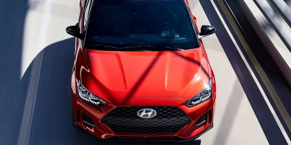 Front view of a red Hyundai driving in sunlight on a modern road