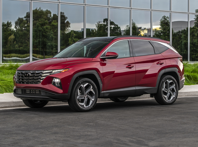 Side view of a red 2023 Hyundai Tucson parked in front of a modern building with reflective glass windows.