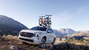 A white 2022 Hyundai Santa Fe being driven with two bikes on the roof in an open field with mountains in the background. | Hyundai dealer in North Little Rock, AR.