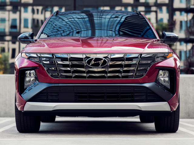 Front view of a red 2023 Hyundai Tucson parked under modern architecture, highlighting bold grille and design