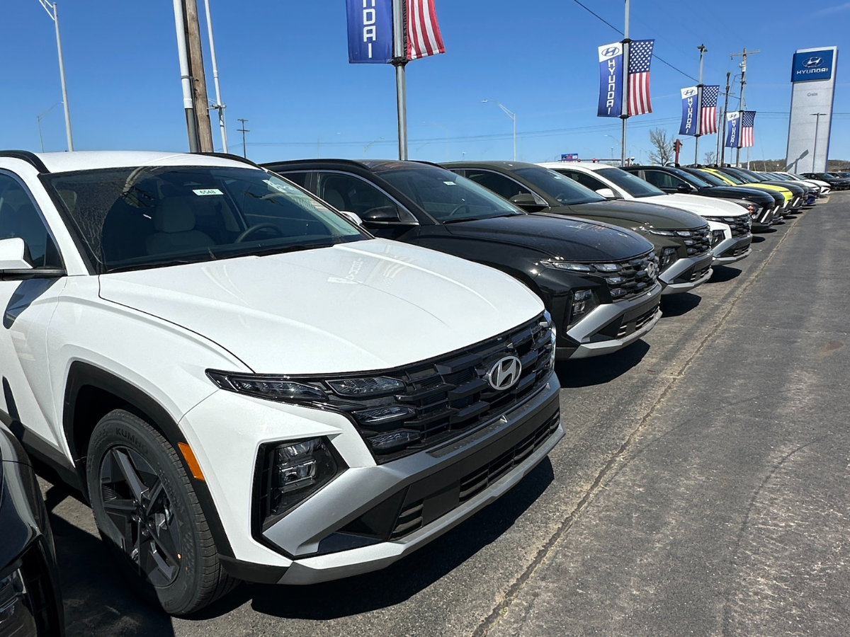 A row of new 2024 Hyundai SUVs, including Tucson models, lined up on the lot at Crain Hyundai of Fort Smith under sunny skies with American flags and Hyundai banners flying above.