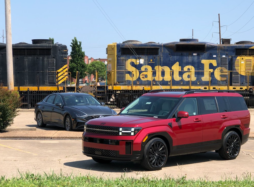 Red Hyundai SUV parked near a train with a black Hyundai sedan in the background