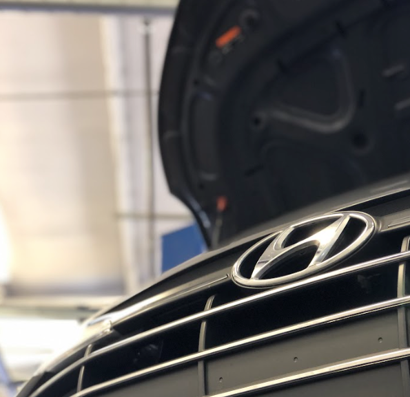 Close-up of Hyundai logo on vehicle grille with hood open in service center