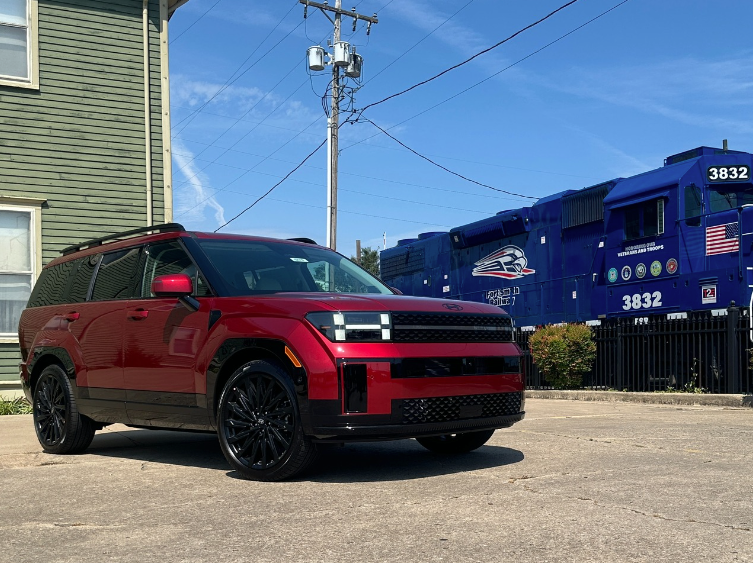 A red Hyundai SUV parked in front of a patriotic blue freight train in Fort Smith, Arkansas, under a clear fall sky.