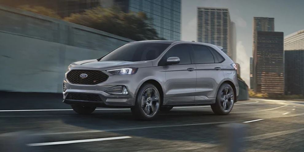 A silver 2023 Ford Edge being driven on the road with buildings in the background. | Ford service in Jacksonville, AR.