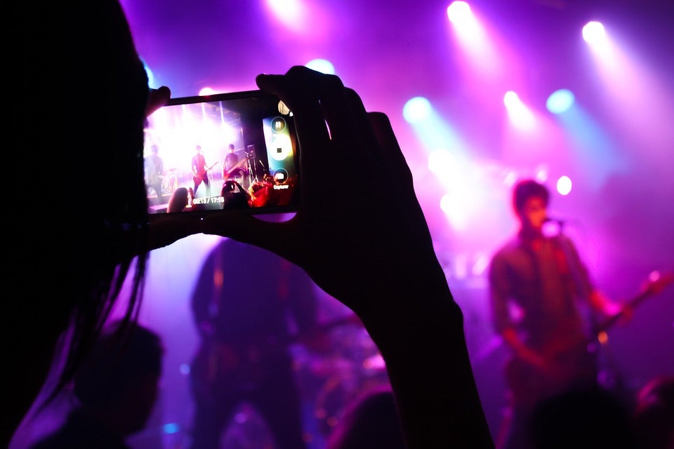 Close view of a phone being held recording a live performance of a band. | Live music around Little Rock, AR.