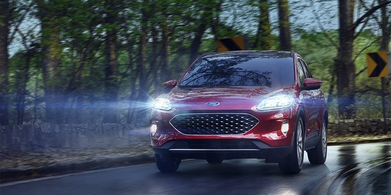 A red 2021 Ford Escape with headlights on being driven on a road. | Ford dealer in Little Rock, AR.