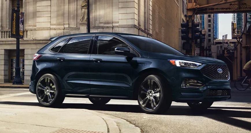 A dark blue 2022 Ford Edge being driven on the road with buildings in the background. | Ford dealer in Little Rock, AR.