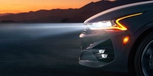 Profile view of the front of a white 2022 Kia K5 with the headlights on. | Kia dealer in Sherwood, AR.