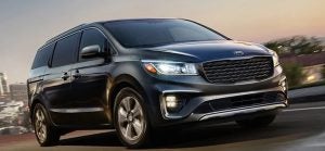 A black 2019 Kia Sedona being driven on the highway with tall buildings in the background. | Kia dealer in Sherwood, AR.