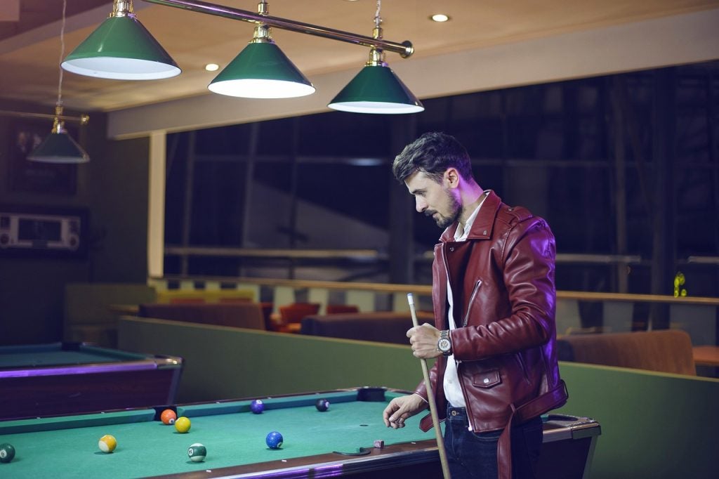 A man holding a pool stick beside a pol table. | Things to do around Conway, AR | Crain Kia of Conway
