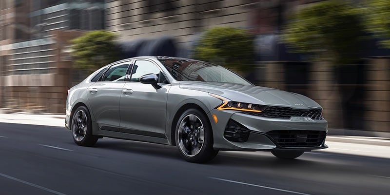 A light gray 2022 Kia K5 being driven on the road. | Kia dealer in Conway, AR.
