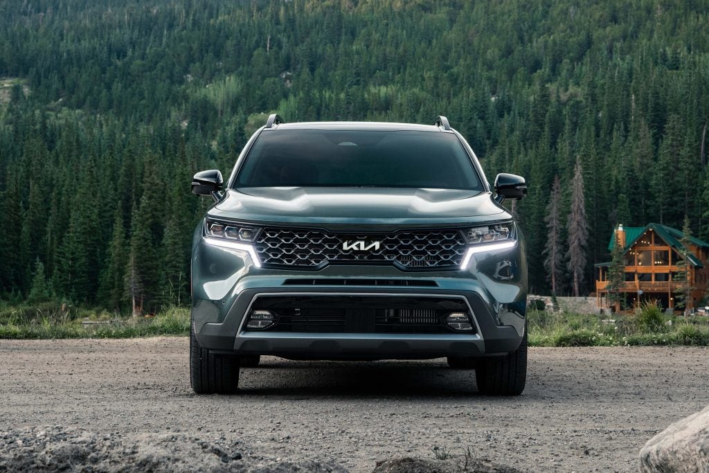 Front view of a dark green 2022 Kia Sorento parked with a cabin and aa multitude of trees far off in the background. | Kia dealer in Conway, AR.