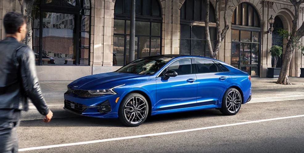 A royal blue 2022 Kia K5 parked on the street in front of a building. | Kia dealer in Bentonville, AR.