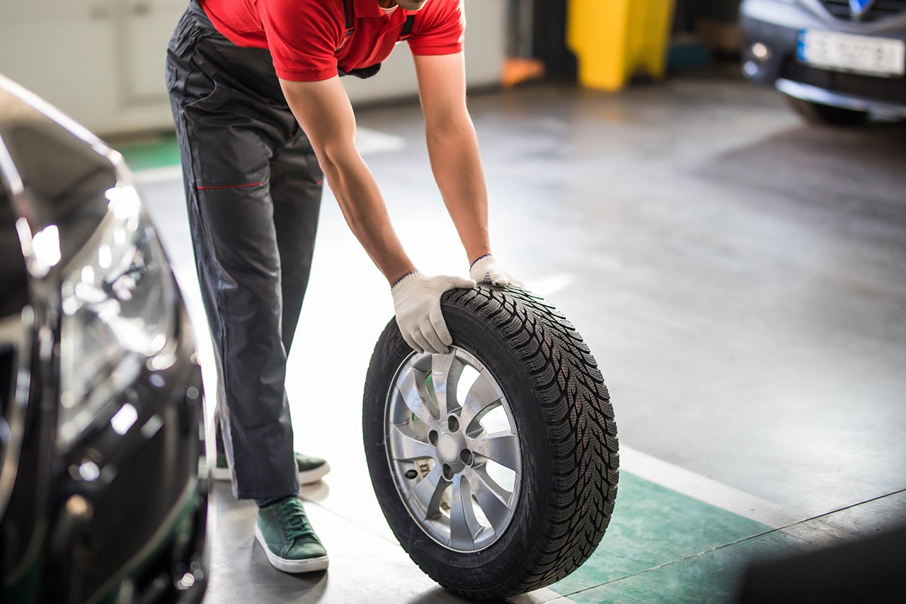 Man auto mechanic carry tires in garage. disc brake on car in process of new tire replacement