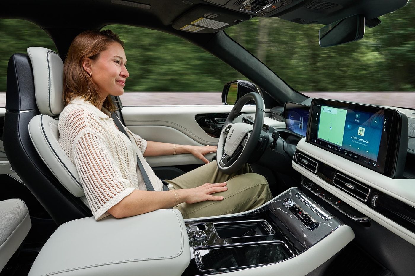 Woman smiling in the front seat of a Lincoln Aviator with her hands off the wheel on a highway