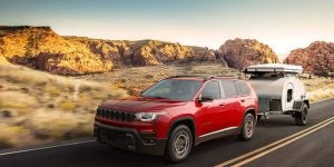 A red Jeep SUV towing a small trailer on a road.