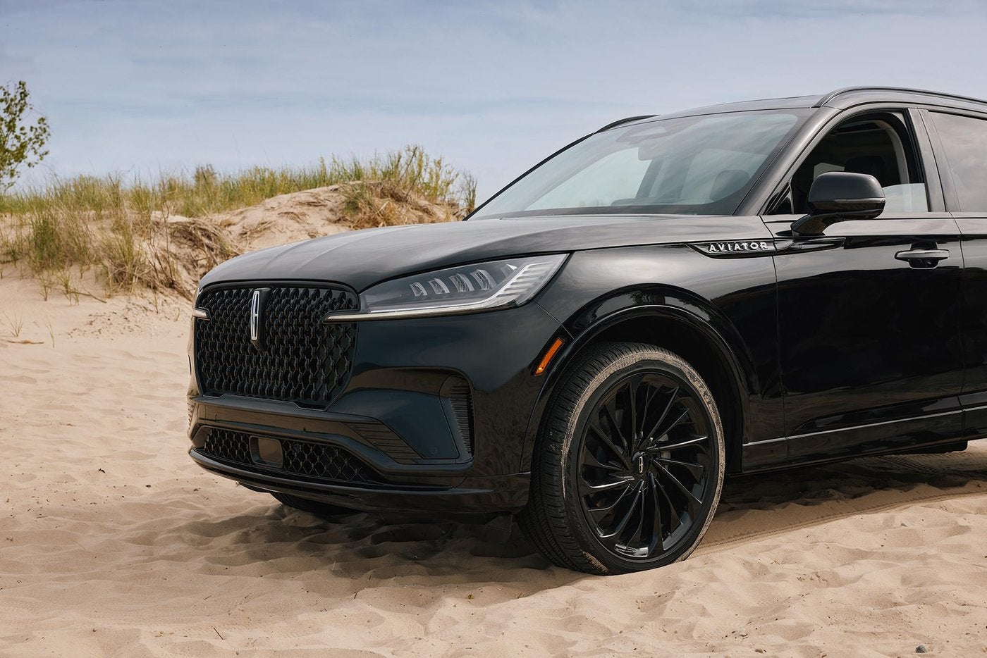 Black Lincoln Aviator parked on sand near tall beach grass in the sun