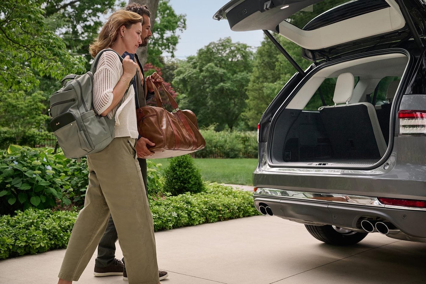 Couple carrying bags toward the open liftgate of a silver Lincoln Aviator