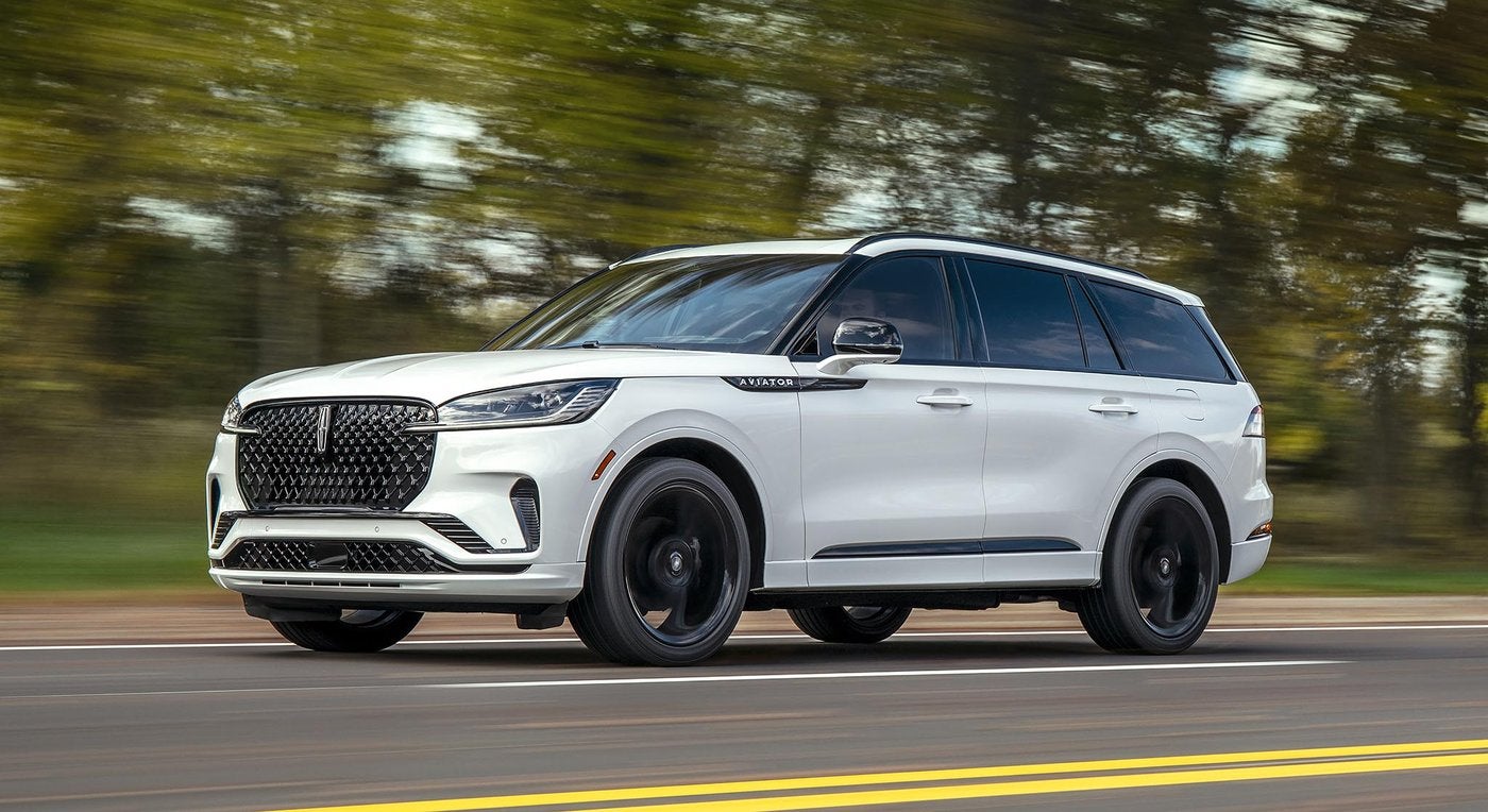 White Lincoln Aviator with black wheels driving on a tree lined road