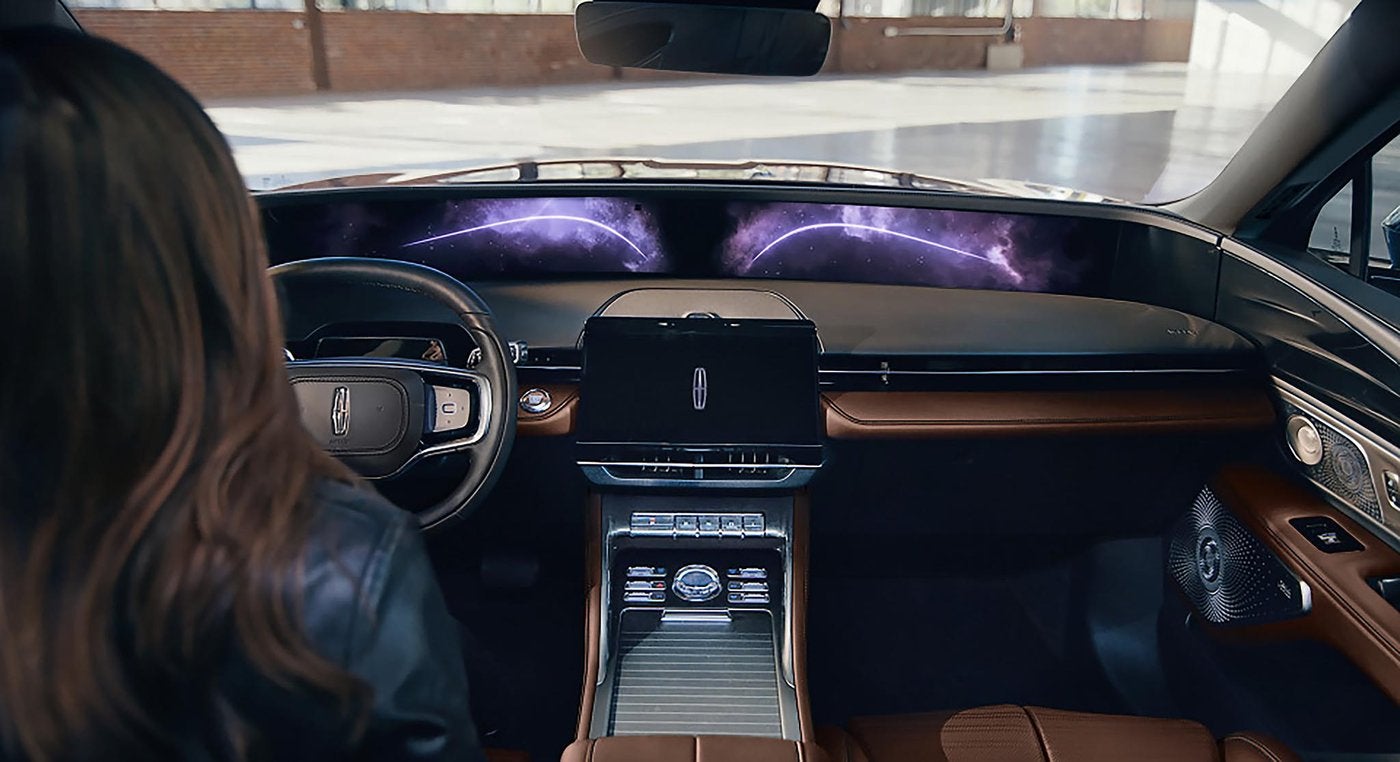Driver seated in a Lincoln Nautilus with the panoramic display lit across the dash